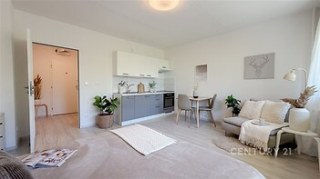 Světlý obývací pokoj s moderní kuchyní, parketová podlaha, velká okna, světlý nábytek, útulná atmosféra.