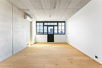 Světlý obývací pokoj s parketovou podlahou a velkými okny, moderní vzhled s betonovým stropem.