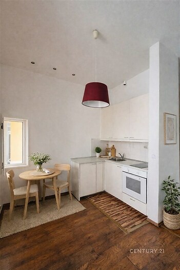 Kompaktní kuchyň s dřevěnou podlahou, moderní bílou linkou a vestavěnými spotřebiči, světlý interiér s jídelním koutem a dekorací.