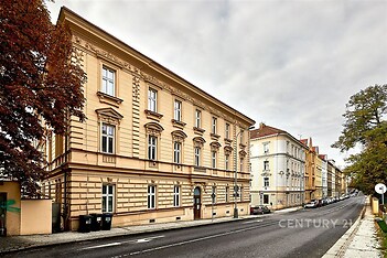 Historická fasáda bytového domu s tradičními architektonickými prvky na klidné ulici, renovovaný exteriér s okny do ulice, udržované okolí.