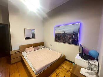 Prostorná ložnice s dřevěnou podlahou a moderním osvětlením, vybavená vestavěnou skříní a velkou postelí, nabízí komfort a styl.