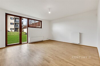 Světlý obývací pokoj s parketovou podlahou a velkými okny, které vedou na zahradu, moderní styl a čisté linie.