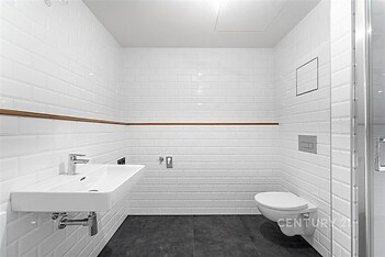 Moderní koupelna s bílými obklady, závěsnou toaletou a umyvadlem. Kombinace dlažby na podlaze a čistý design vytváří světlý prostor.