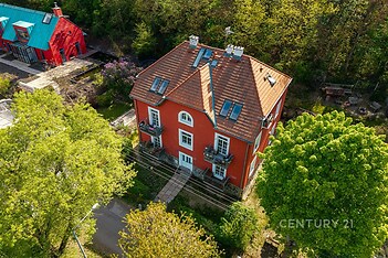 Červená vila s klasickou fasádou, novou střechou a terasou, obklopená zelení, nabízí klidné bydlení v soukromí blízkosti lesa.