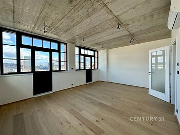 Průmyslový obývací pokoj s dřevěnou parketovou podlahou a betonovým stropem nabízí velká okna s panoramatickým výhledem na město