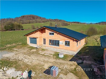 Nedokončený rodinný dům s hrubou stavbou a betonovou střešní krytinou v malebné venkovské krajině, ideální pro rekonstrukci.