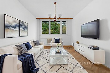 Světlý obývací pokoj s parketovou podlahou, velkými okny a moderním zařízením, nabízí útulný a elegantní prostor pro relaxaci.