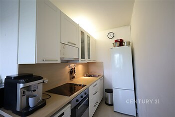 Úzká kuchyň s bílými skříňkami, vestavěnými spotřebiči a světlou pracovní deskou, moderní design, světlé stěny.