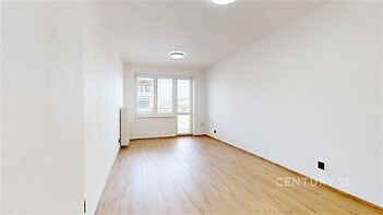 Světlý obývací pokoj s parketovou podlahou, velká okna zajišťují dostatek přirozeného světla, moderní jednoduchý styl v neutrálních tónech.