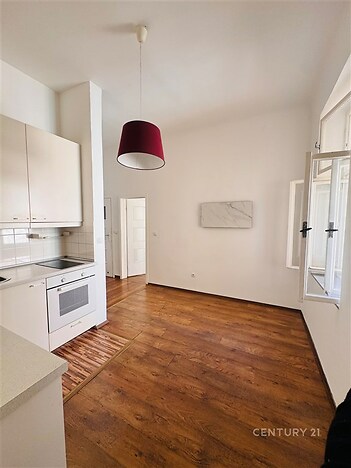 Kuchyňský kout s dřevěnou podlahou, světlými skříňkami a velkým oknem, moderní spotřebiče zajišťují pohodlí a útulnost.