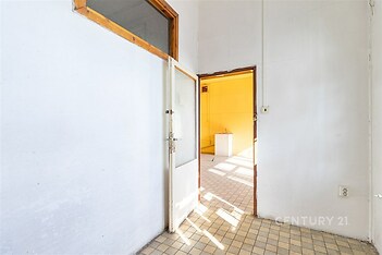 Vstupní hala s dlažbou, vysoké stropy a dveře vedou do světlé místnosti s velkými okny, ideální pro moderní rekonstrukci.