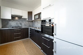 Moderní kuchyň s tmavou dřevěnou linkou, vestavěnými spotřebiči a světlou dlažbou vytváří elegantní a praktický prostor pro vaření.
