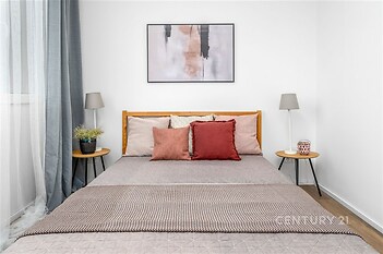 Prostorná ložnice s parketovou podlahou, velkými okny a moderním nábytkem, vytváří světlý a útulný prostor pro relaxaci.