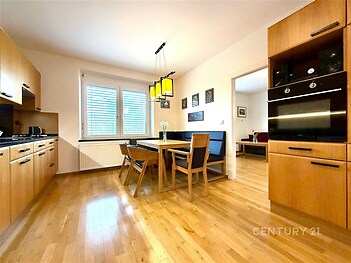 Moderní kuchyň s parketovou podlahou, vestavěnými spotřebiči a velkými okny nabízí světlý a prostorný interiér ideální pro rodinné vaření.