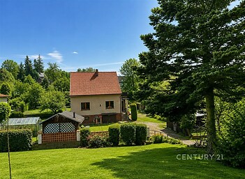 Rodinný dům s červenou střechou obklopený zelení v klidné lokalitě, zahrada s trávníkem a vzrostlými stromy, ideální pro rodinný život