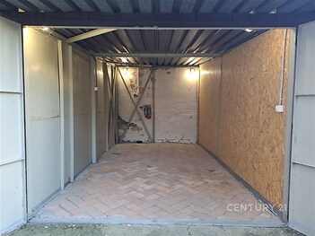 Jednoduchá garáž s průmyslovým stropem, dlážděnou podlahou a dřevěnými obklady, vhodná pro uskladnění nebo parkování vozu.