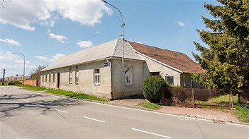 Tradiční vesnický dům s šikmou střechou a velkou zahradou, umístěný u hlavní silnice, vhodný k částečné rekonstrukci nebo úpravám.