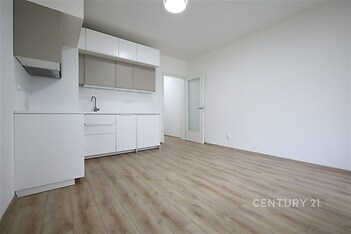 Moderní kuchyň s parketovou podlahou, bílými skříňkami a čistými liniemi, světlý interiér s velkou přívodní skleněnou dveří pro přirozené světlo.