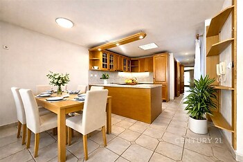 Prostorná kuchyň s dlažbou, moderními dřevěnými skříněmi a velkým jídelním stolem, nabízí světlý interiér a elegantní vybavení.