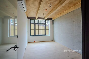 Prázdná místnost s velkými okny, dřevěným stropem a parketovou podlahou, moderní styl a přirozené osvětlení.