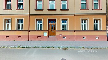 Historická fasáda bytového domu s dřevěnými dveřmi a velkými okny, udržovaná architektura a klidná lokalita poblíž centra.