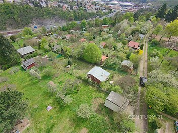 Zahrádkářská kolonie s rozlehlými zelenými pozemky, několika chatami a stromy, v klidné oblasti s výhledem na město.