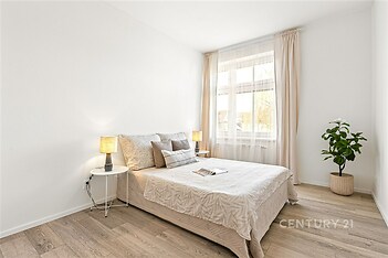 Světlá ložnice s dřevěnou podlahou, velkým oknem a moderním designem nabízí příjemné a útulné prostředí pro relaxaci.