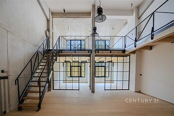 Velký industriální obývací pokoj, parketová podlaha, ocelové schodiště, vysoké stropy a prosklená přepážka, moderní styl.