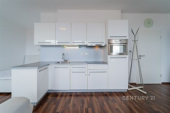 Moderní kuchyň s bílými lesklými skříňkami, vestavěnou troubou a parketovou podlahou, prostorný design pro pohodlné bydlení.