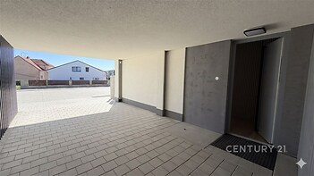 Zastřešené venkovní stání s moderní dlažbou a čistými liniemi nabízí bezpečné parkování a vstup do budovy.