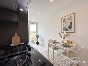 Kompaktní jídelní kout s moderním nábytkem, světlou dlažbou a velkým oknem. Minimalistický styl a světlé vybavení vytvářejí elegantní atmosféru.