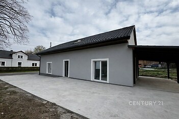 Moderní rodinný dům s šedou fasádou a velkými francouzskými okny, dlážděný prostor v klidné oblasti, vhodný pro pohodlné bydlení.