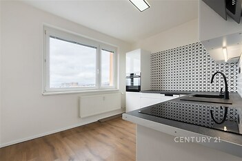 Moderní kuchyň s parketovou podlahou, velkým oknem a černobílými obklady. Světlý prostor s vestavěnými spotřebiči.