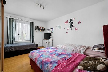 Světlá ložnice s parketovou podlahou, velkými okny a moderním nábytkem, ideální pro pohodlné bydlení.