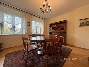 Jídelna s parketovou podlahou, dřevěným nábytkem a velkými okny, která propouštějí dostatek světla, vytváří útulný prostor pro rodinné stolování.