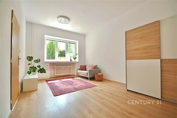 Světlý obývací pokoj s parketovou podlahou, velká okna, moderní vestavěné skříně a minimalistický styl nabízí útulný prostor pro bydlení.