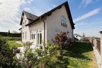 Exteriér rodinného domu s moderní fasádou, zahrada s terasou a upraveným trávníkem, prostorný pozemek, klidná lokalita.