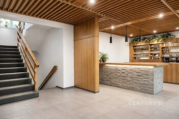 Recepční prostor s moderním designem, dřevěným obložením a kamenným pultem, doplněný kovovými svítidly a parketovou podlahou pro stylový vzhled.