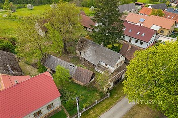 Venkovský pozemek se starými budovami, červená střecha, okolní zeleň, klidná lokalita. Potenciál pro rekonstrukci či nový výstavbu.