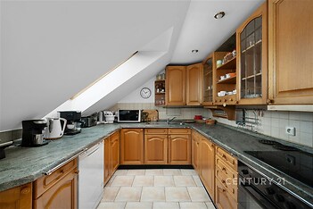 Podkrovní kuchyň s dřevěnými skříňkami, dlažbou a velkým střešním oknem, které zajišťuje dostatek světla, působí útulně a moderně.