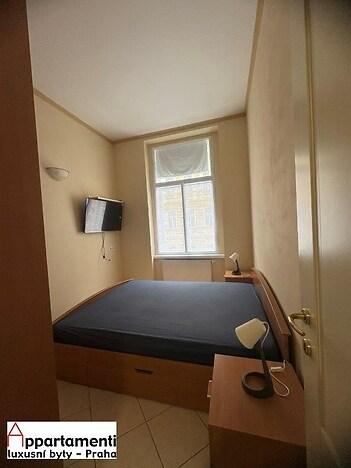 Útulná ložnice, dlažba na podlaze, velké okno, moderní osvětlení, vestavěná skříňová úložná řešení pro maximální prostor.