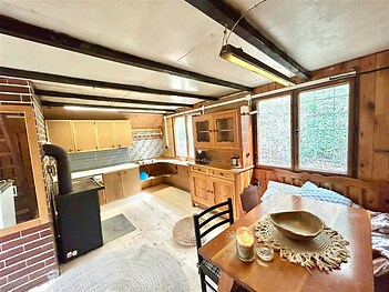 Rustikální kuchyň se dřevěnými obklady, velkými okny a krbovými kamny, nabízí útulný prostor pro vaření a relaxaci.