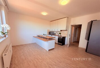 Světlá kuchyň s parketovou podlahou, vestavěné skříně a moderní spotřebiče, vedle velkého okna, nabízí pohodlí a eleganci.