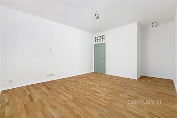 Prázdný obývací pokoj s parketovou podlahou, bílými stěnami a pastelovými dveřmi, minimalistický design, připravený k okamžitému nastěhování.