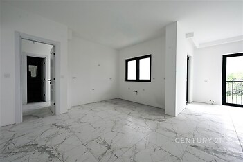 Světlý obývací pokoj s moderní dlažbou a velkými okny, které umožňují dostatek přirozeného světla, ideální pro otevřený a vzdušný interiér.