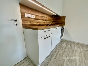 Moderní kuchyň s dřevěnými detaily, světlá parketová podlaha, vestavěné spotřebiče, čistý design.