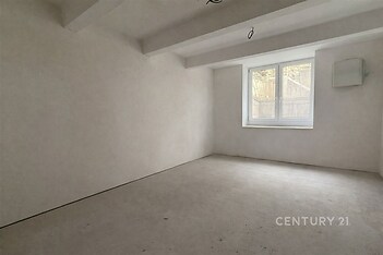 Prázdný pokoj s bílými stěnami, betonová podlaha a velká okna, rekonstruovaný prostor, připravený k úpravám.