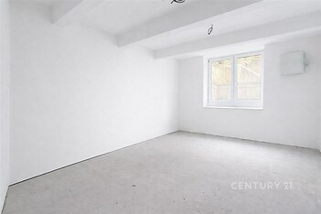 Rekonstruovaný světlý pokoj s bílými stěnami, betonovou podlahou a velkým oknem poskytujícím přirozené světlo.