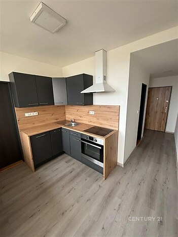 Moderní kuchyň s laminátovou podlahou, tmavými skříňkami a dřevěným obkladem. Vybavená sporákem a digestoří, moderní design.