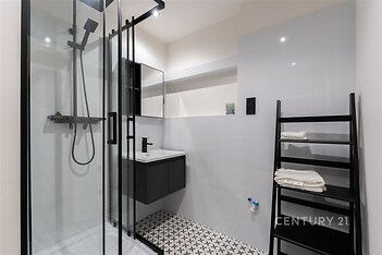 Moderní koupelna s proskleným sprchovým koutem, bílými dlaždicemi a dlažbou s geometrickým vzorem, elegantní černé prvky dodávají styl.